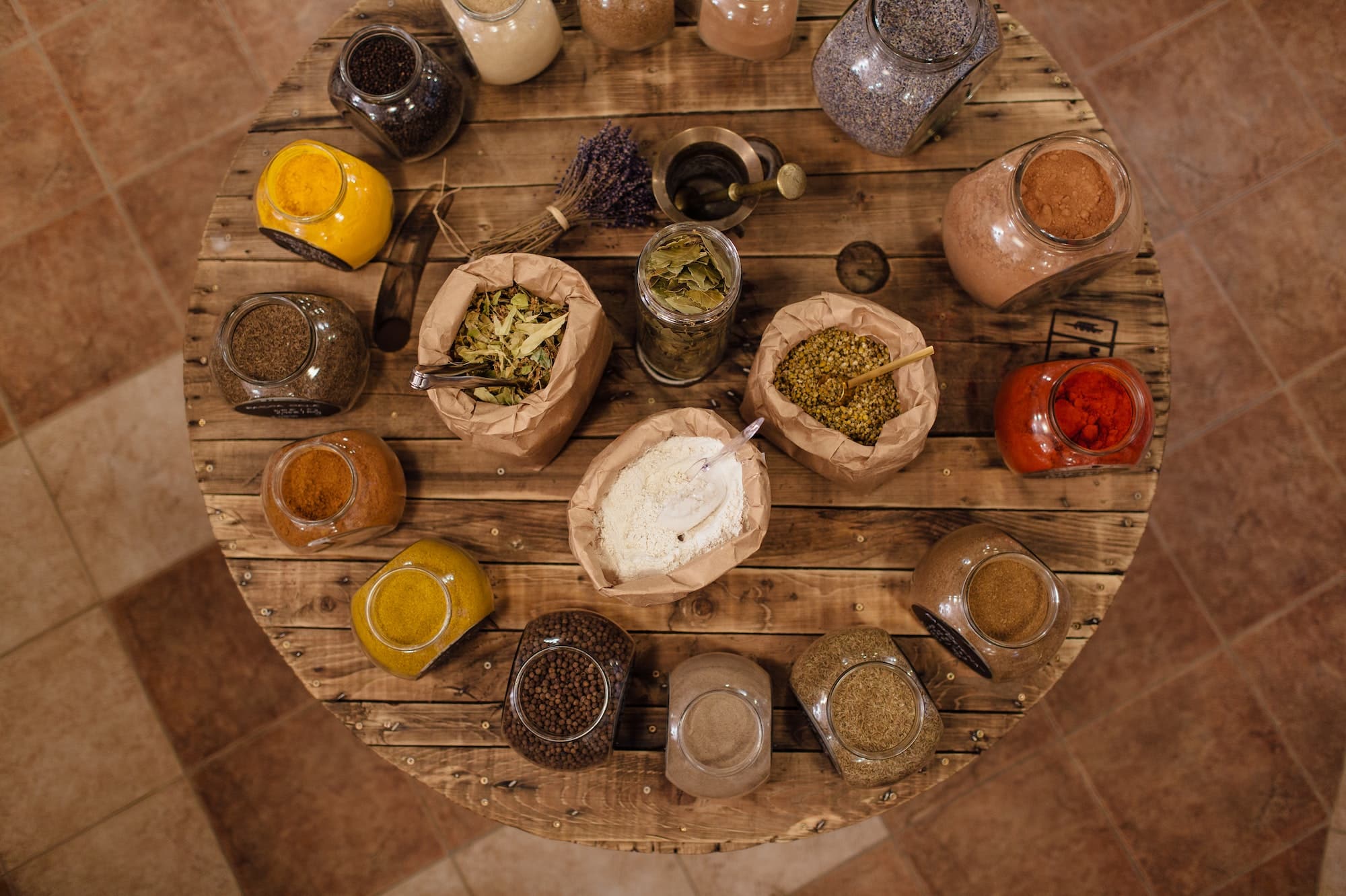 Variety of colorful dried herbs and spices displayed on round wooden table in plastic free store.